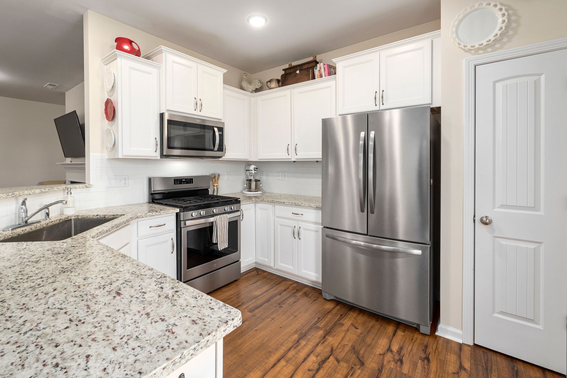 Bright modern kitchen featuring white cabinets and stainless steel appliances, including a refrigerator and stove.